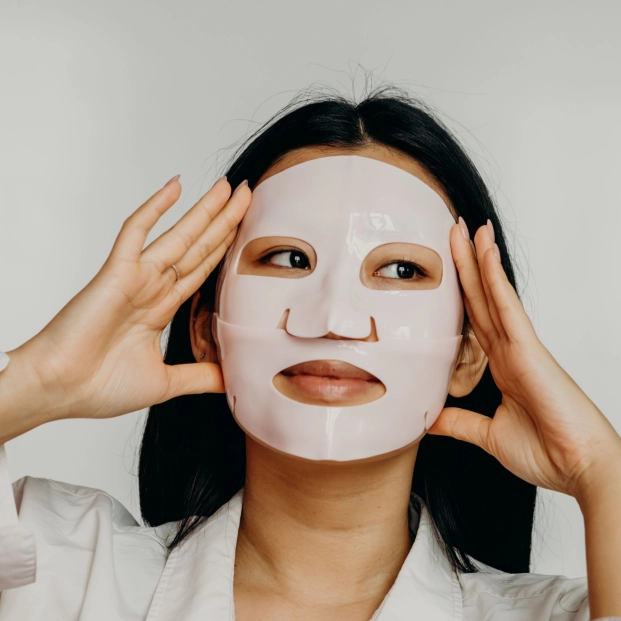 etalle de una modelo aplicando una mascarilla coreana de hidrogel transparente sobre la piel limpia e iluminada